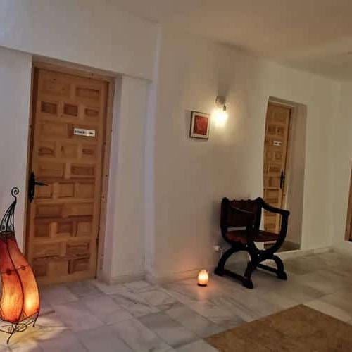 Valgete seinte ja marmorpõrandaga koridoris on kolm puidust ust, väike tool ning laud raamatute ja vaasiga - see loob kutsuva majutusatmosfääri, mida suurendavad dekoratiivne põrandalamp ja ümberringi paigutatud küünlad.